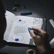 Person using Schneider One Business 0.6MM Roller Ball Pen to write in a notebook showcasing designs for August.
