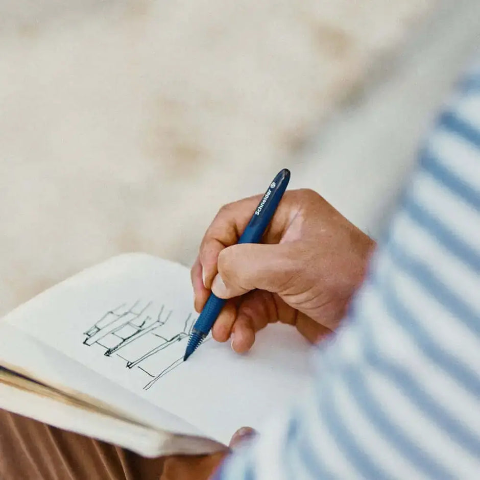 Person using Schneider One Business 0.6MM Roller Ball Pen to sketch in a notebook.