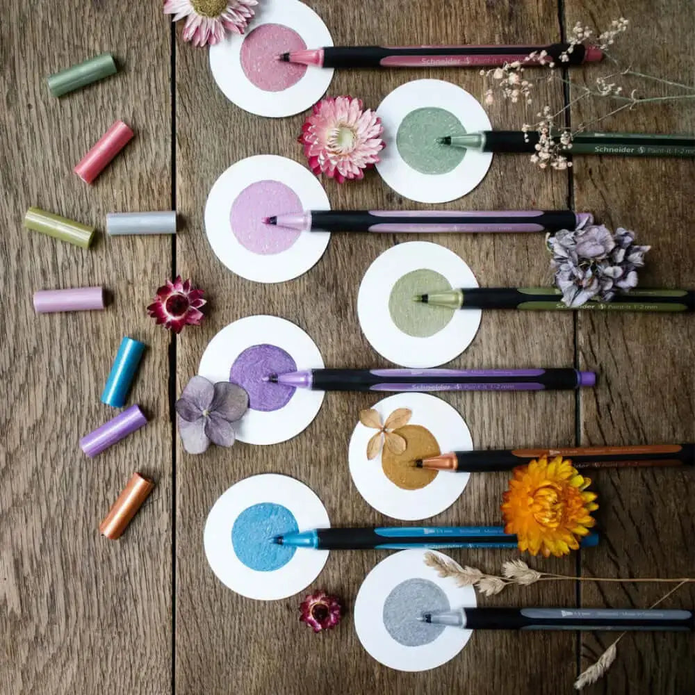 Schneider Paint-it 020 Metallic Liner Pens displayed with nature-themed decorations on a wooden surface.