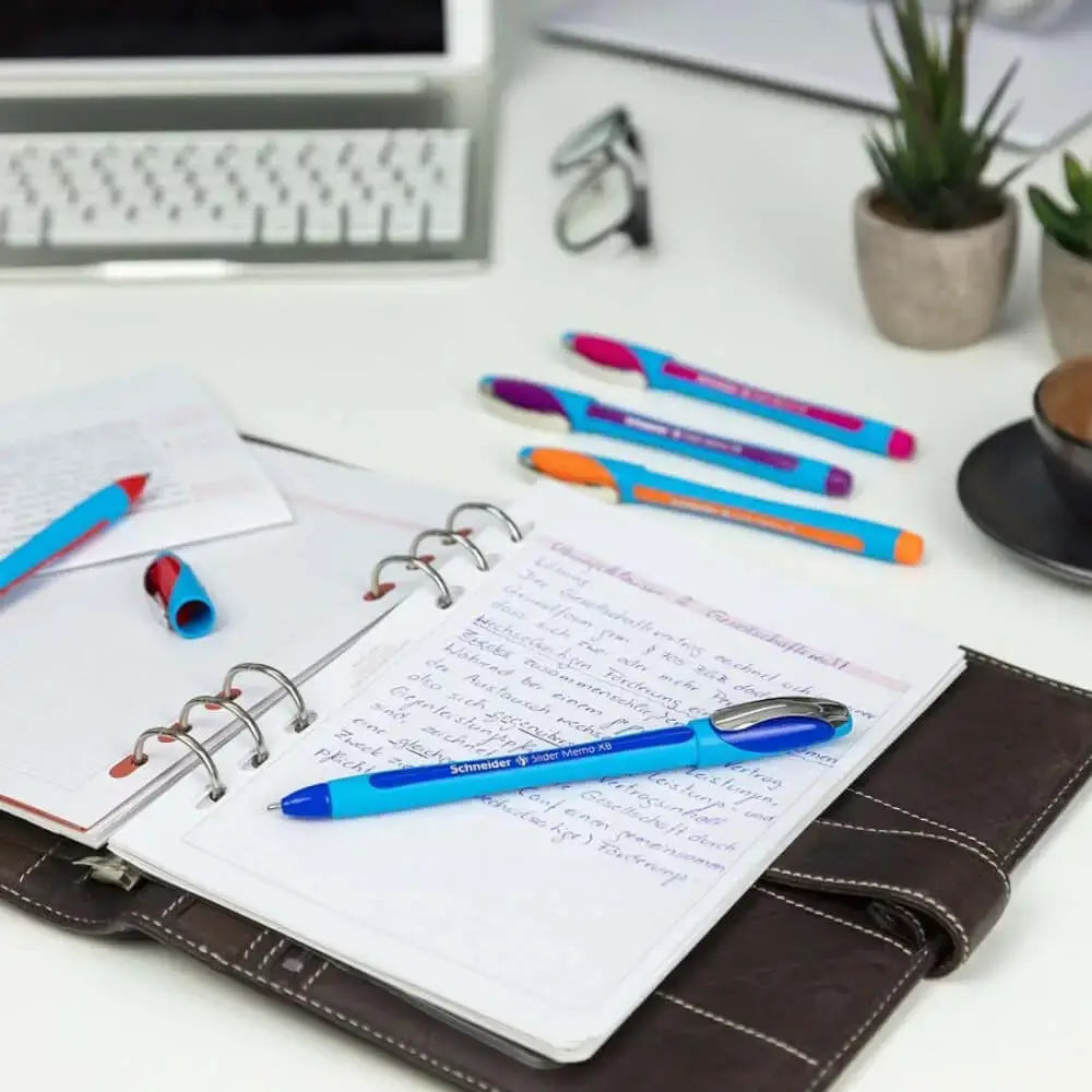 Schneider Slider Memo XB Ball Point Pen on an open notebook with other pens and stationery.